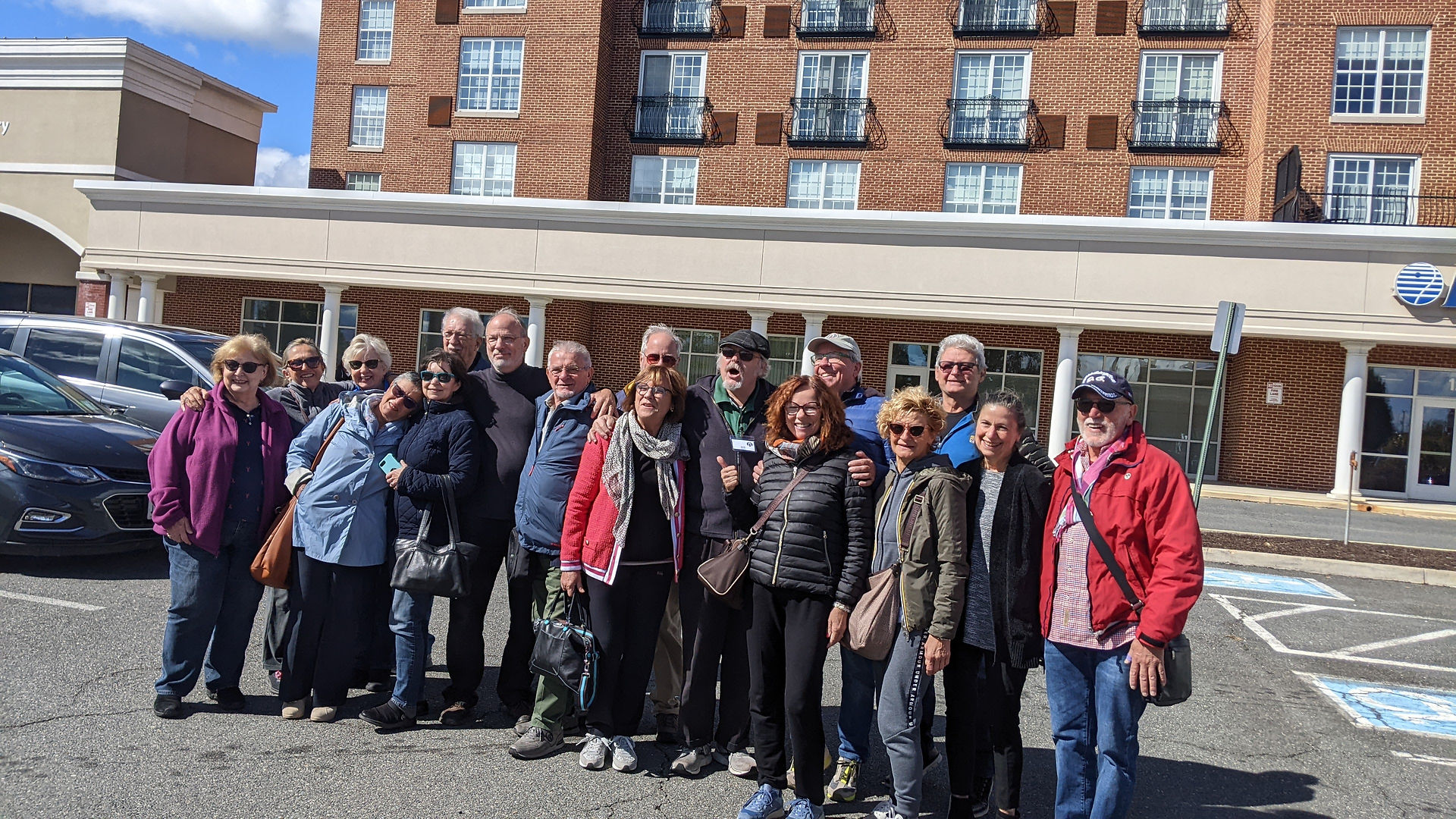 Group of diverse tourists smiling outside a large brick hotel building.