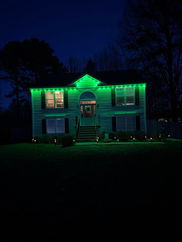 Green permanent holiday lights on a two-story home at night
