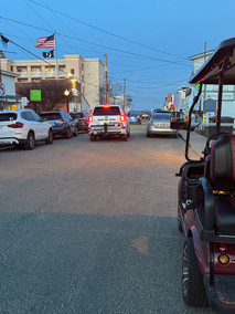 Street with parked cars, buildings, and a golf cart at dusk