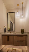 Modern light wood vanity, concrete counter, gold fixtures, dark framed mirror.