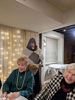 La Befana holding a basket, visiting smiling women at event.