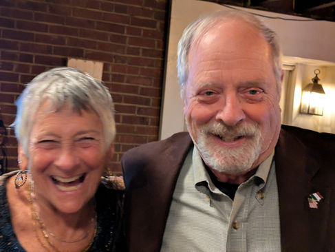 Happy elderly couple smiling broadly together indoors with brick wall.