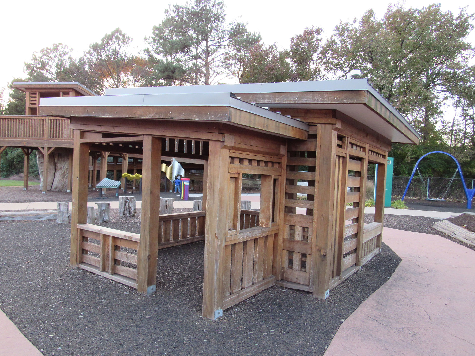 Wooden play structure with metal roof in a children's playground setting.