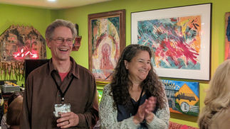 Joyful man laughing alongside woman clapping amidst vibrant artwork.