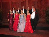 Group of singers in formal wear pose for a photo together.