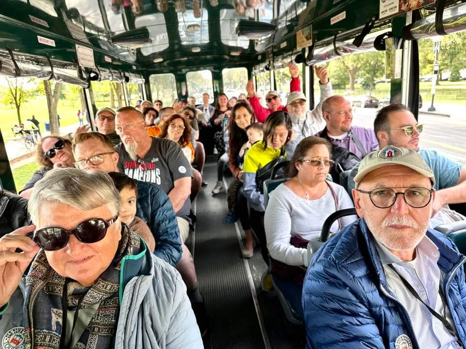 Diverse group of people riding on a green open-air tour bus.