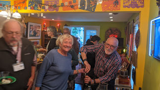 Smiling woman watches man open wine at festive indoor gathering.