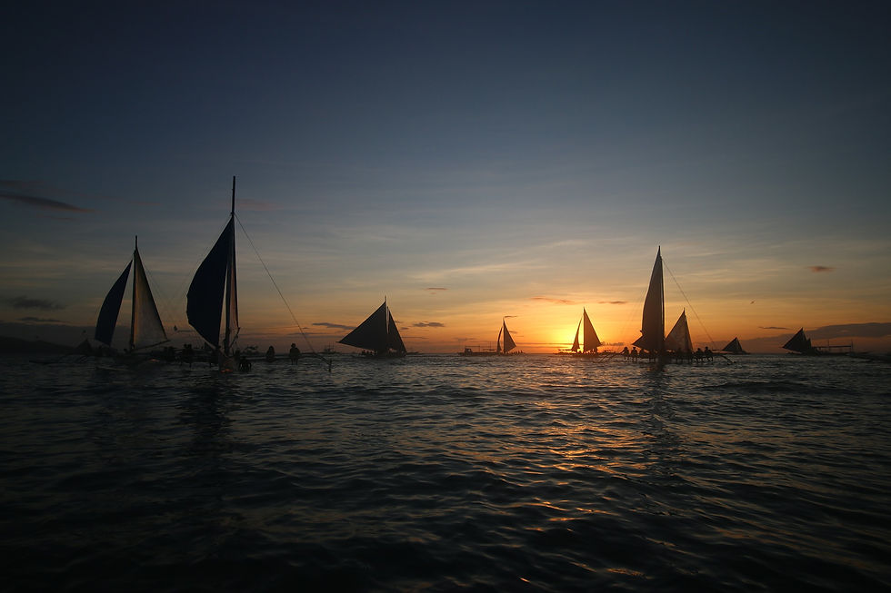 sailboats congregating on ocean as sun sets/rises