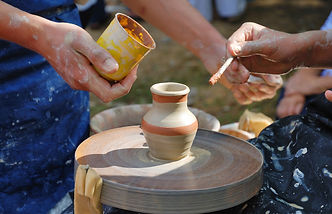 two people shaping and painting a clay pot, a metaphor for creativity