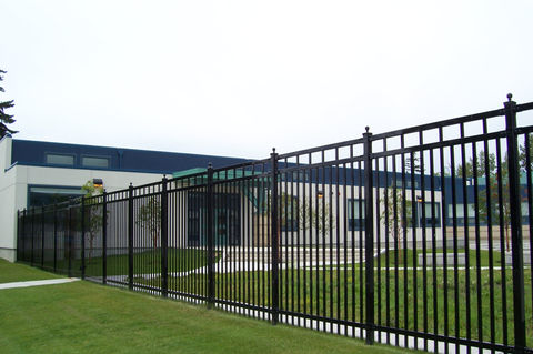 Black metal fence surrounding a building with green grass and overcast skies.