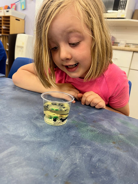 Curious blonde girl intently observes layered contents within a small cup.
