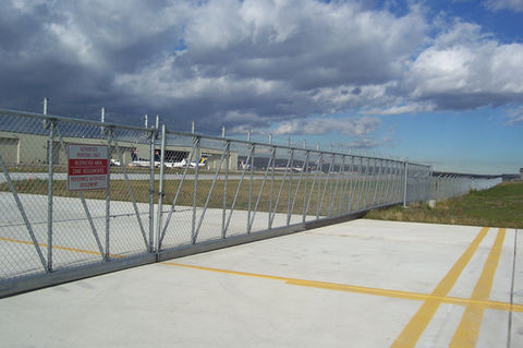 Chain link fence with gate, concrete, and cloudy sky in background.