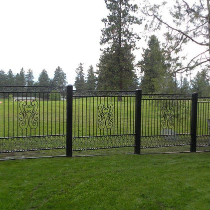 Black wrought iron fence with decorative details in front of a green field.