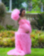 Pregnant woman in a pink maternity gown standing in a garden while cradling her belly.