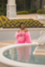 Pregnant woman wearing a pink maternity gown beside an outdoor reflecting pool and decorative fountain.