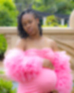Pregnant woman in a bright pink maternity gown posing beside a stone balustrade outdoors.