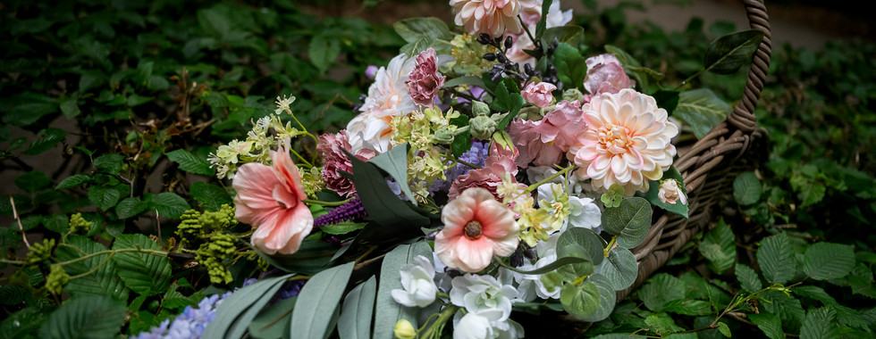 Op de kist ligt een rouwboeket van zijde bloemen, dit is herschikt tot een mooi herinneringsboeket.