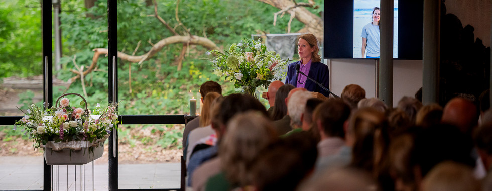 Op de kist ligt een rouwboeket van zijde bloemen, dit is herschikt tot een mooi herinneringsboeket.