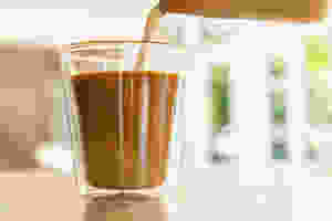 Iced latte milk jug pouring into double walled glass with espresso