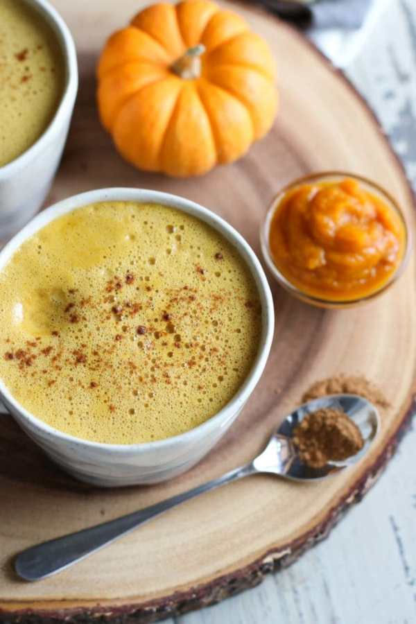 Cup of pumpkin spice coffee resting on a circular chunk of wood with pumpkin, and puree around it