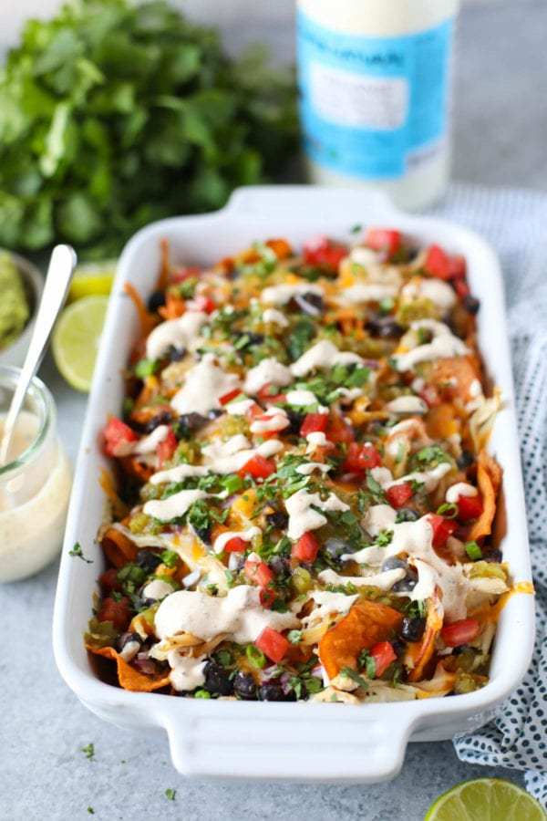 White baking dish filled with Loaded Sweet Potato Nachos with a bottle of Kalona Supernatural Plain Whole Milk Kefir in the background.