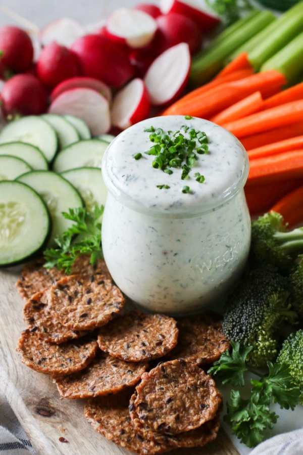 Photo of Healthy Homemade Ranch Dressing in a mason jar topped with fresh chives and surrounded by fresh cut vegetables.