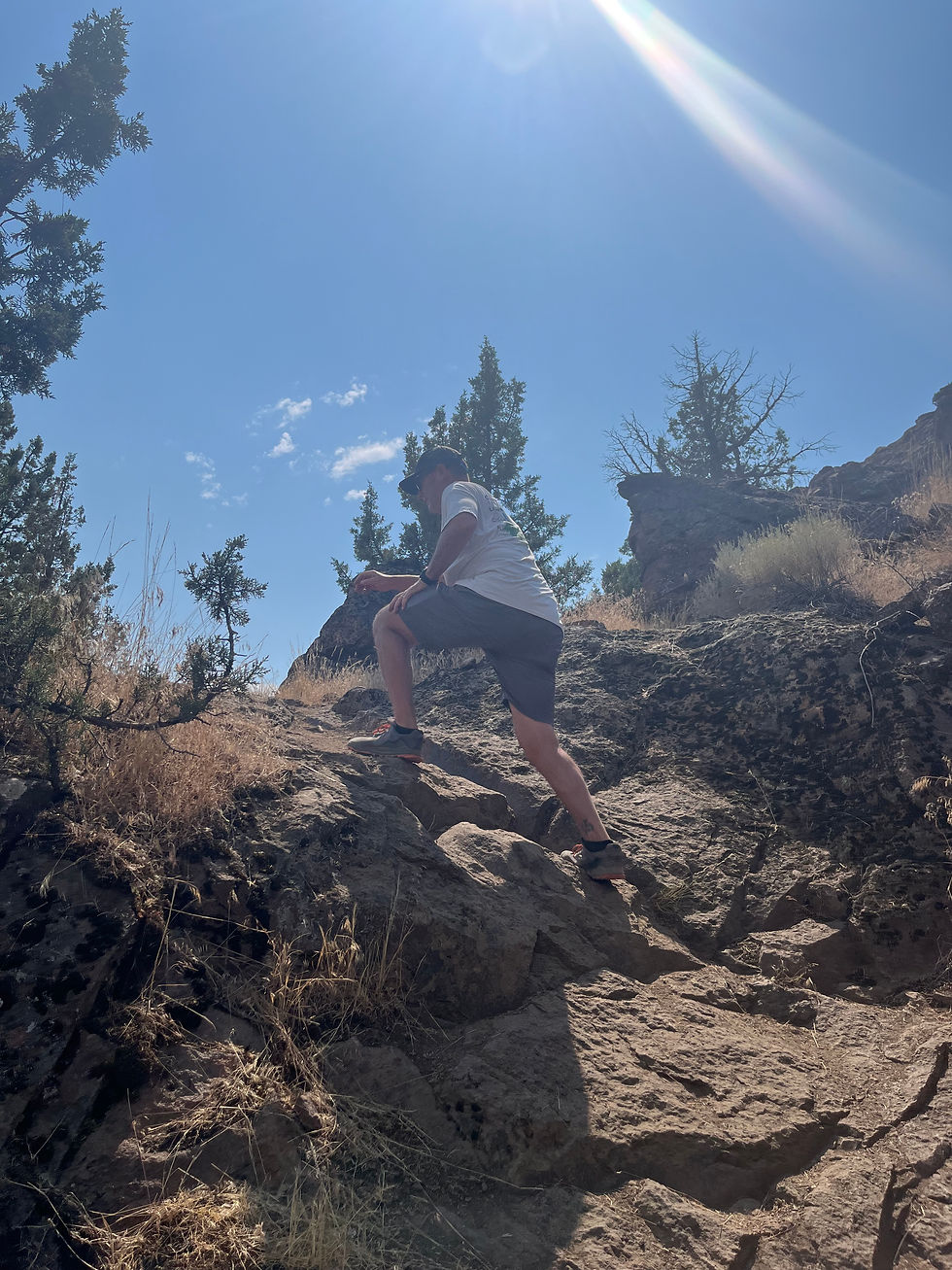 A hiker scrambles up a steep rock face, with a blue sky visible above him.