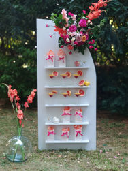 panneau avec etagere pour presenter cocktail colores et fruites pamplemousse et sachets cadeaux invites composition florale destructuree coloree