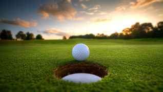 balle de golf juste devant le trou avec un couché de soleil derrière