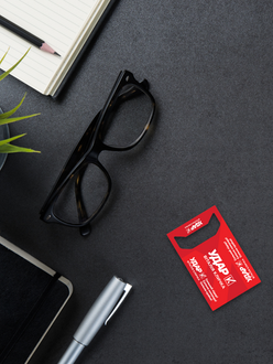 Creative red business card displayed beside glasses, a notebook and pen on a dark office desk