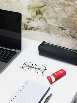Red custom promotional card on a white office desk beside a laptop, glasses and notebook