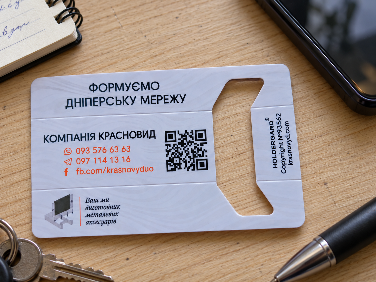 Real Krasnovyd HOLDERCARD promotional card on a working desk with phone, notebook, keys and pen
