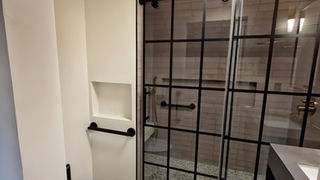 Project Stewardship: A modern walk-in shower featuring a black industrial grid frame and subway tile, illustrating high-end material curation in a luxury renovation.