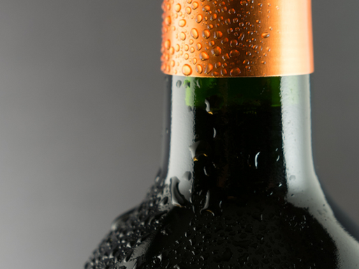 Close-up of a dark glass bottleneck with a copper foil cap and condensation droplets, a visual metaphor for leaders who become the bottleneck in their organization