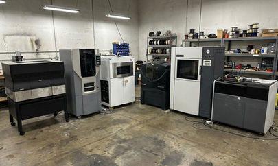 Impressora 3D industrial Stratasys parada em galpão com cobertura de proteção.