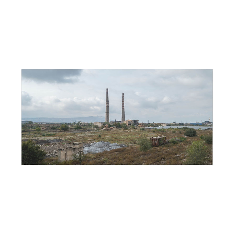 Thumbnail: Two tall industrial chimneys dominate a desolate landscape under a cloudy sky.