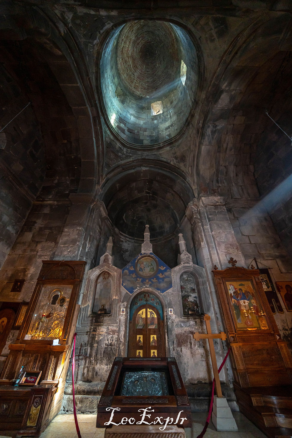 Interior of an ancient church with high dome, icons, and ornate woodwork. Light streams through, creating a serene atmosphere. Gergeti Trinity Church in Georgia.