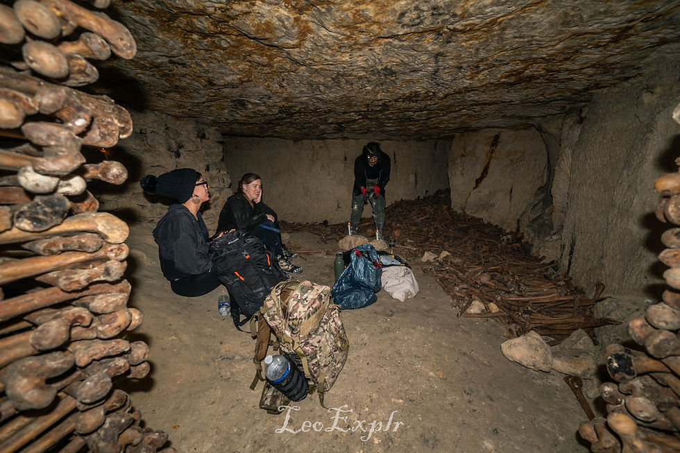 Three explorers with their backpacks in the Paris Catacombs surrounded by bones in a room with low ceiling