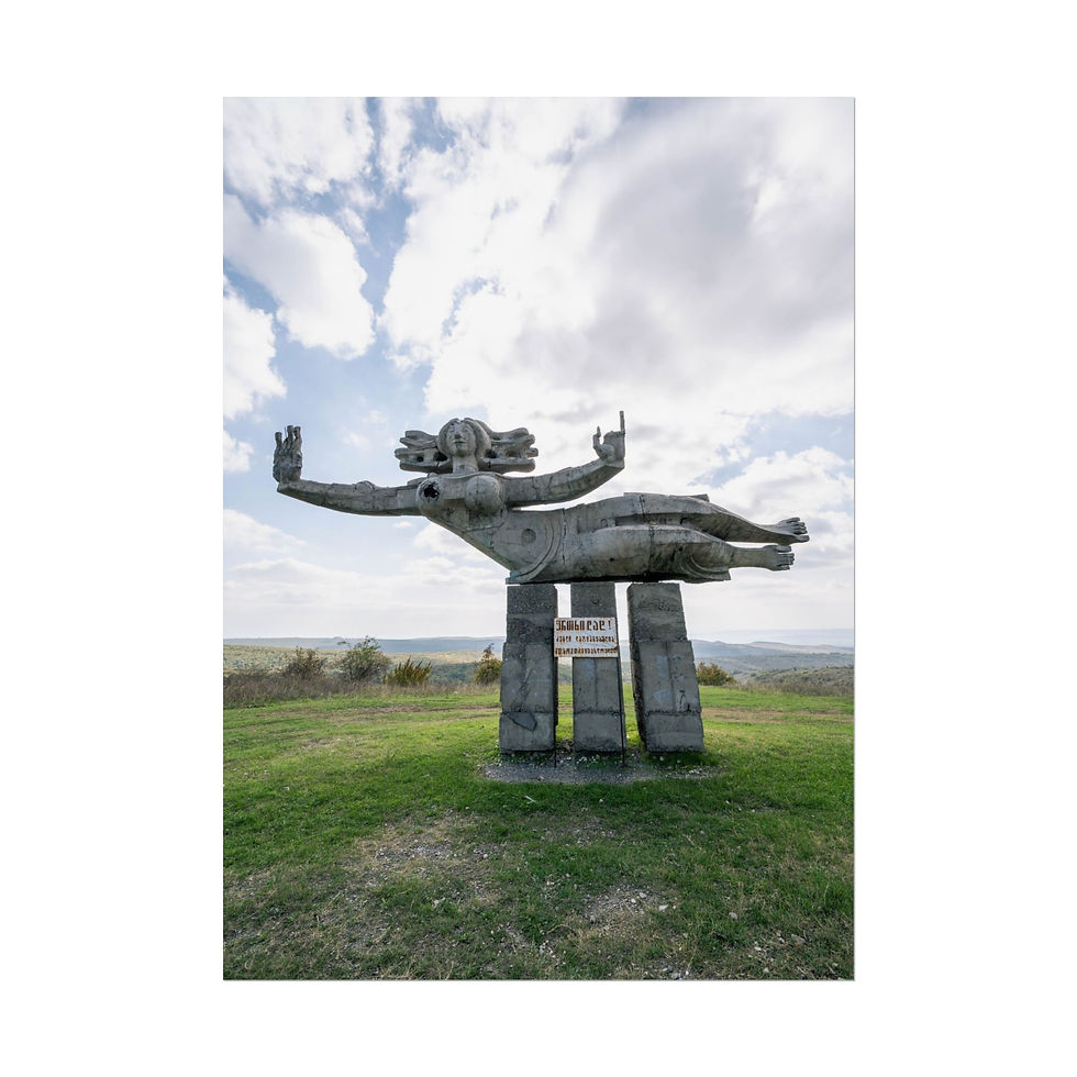 Thumbnail: Large weathered concrete abstract statue on a grassy hill under cloudy sky.