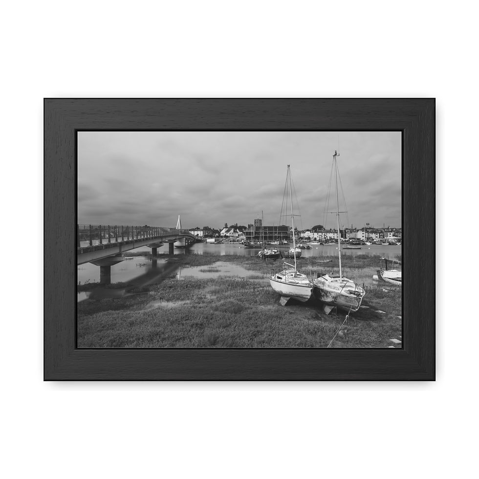 Thumbnail: Black and white boats grounded in mudflats, bridge, distant town, cloudy sky.