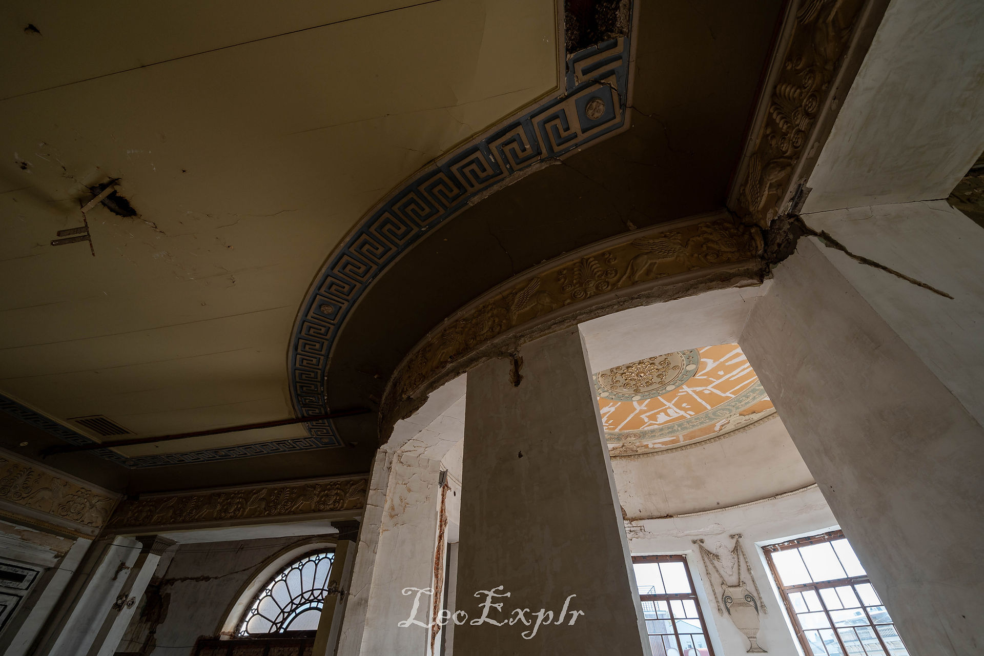 Abandoned Apollo Cinema in Tbilisi, Georgia. A deteriorating ceiling with ornate moldings and peeling paint in an abandoned building, featuring arched windows and a somber, neglected atmosphere.