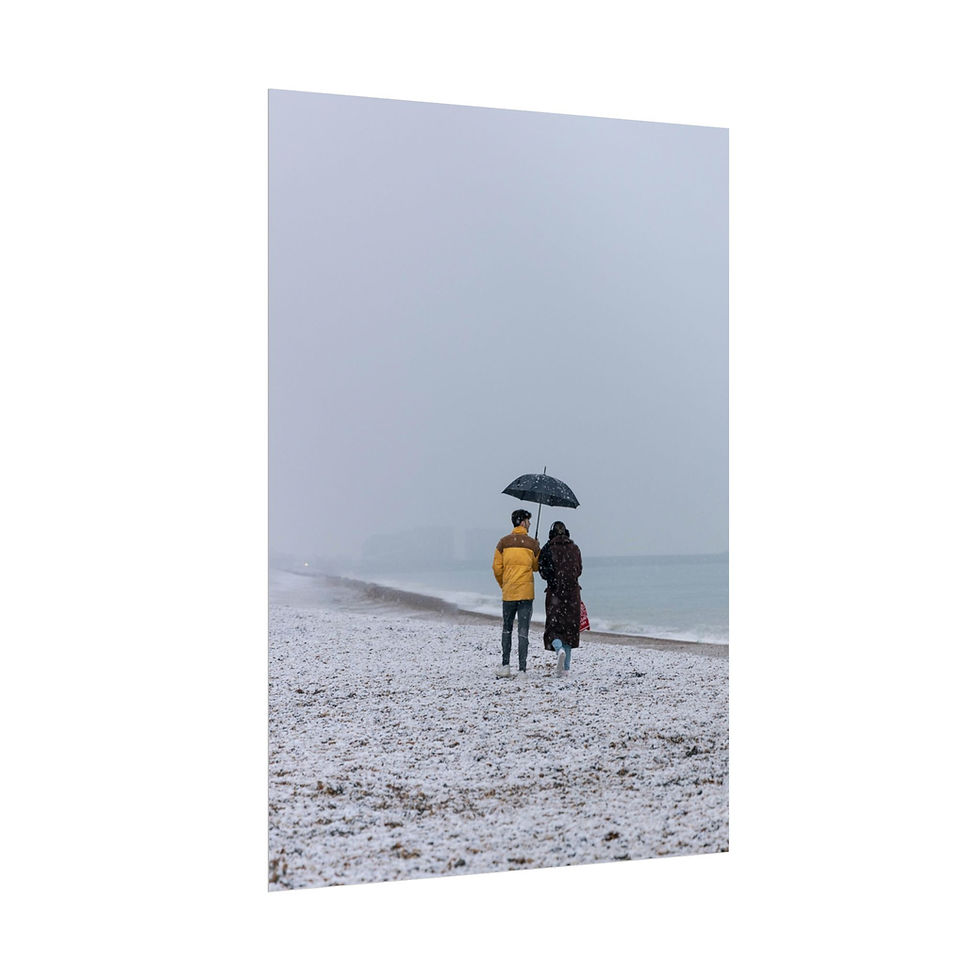 Thumbnail: Two people with umbrella walk on snowy beach beside grey sea.