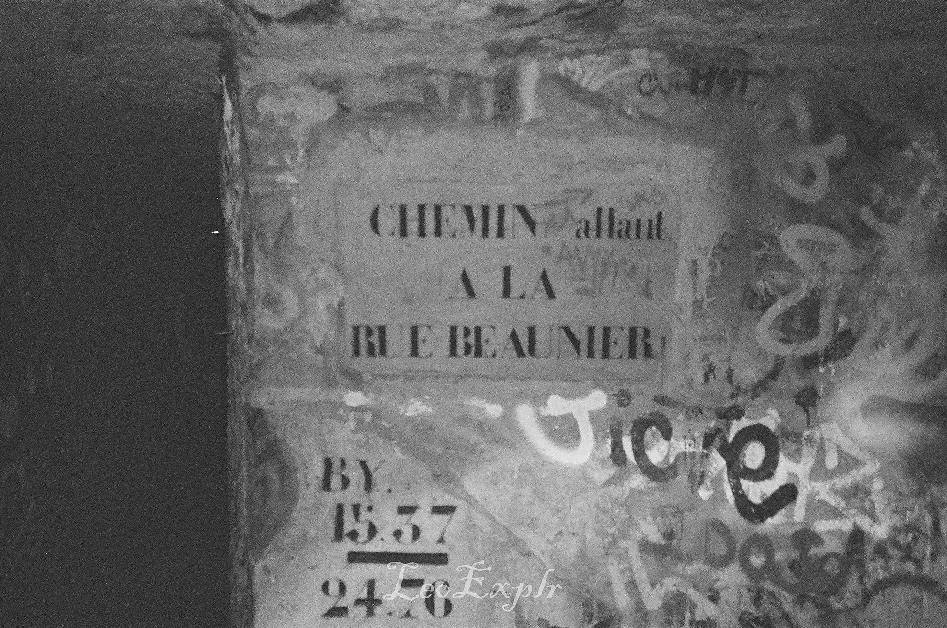 Black and white image of a road sign underground in the Paris Catacombs reads "CHEMIN allant A LA RUE BEAUNIER - BY 1537"