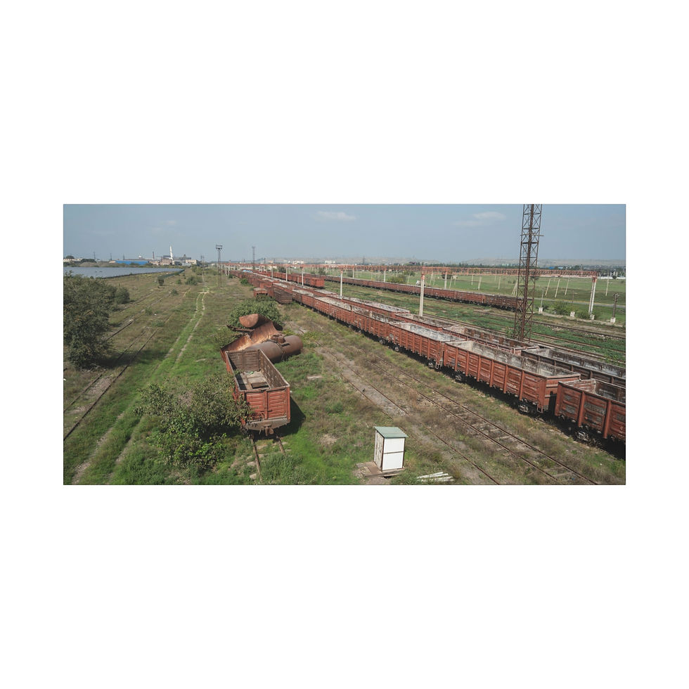 Thumbnail: Long cargo train on tracks next to rusted barge, green embankment.
