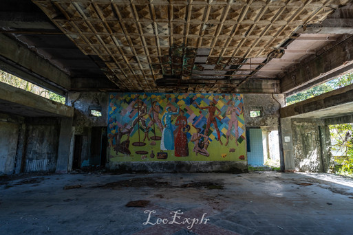 Wine-making mosaic in Hotel Aia in Tskaltubo, Georgia. Abandoned building interior with a colourful mural depicting abstract human figures on a vibrant blue and green wall, surrounded by dilapidated surfaces.