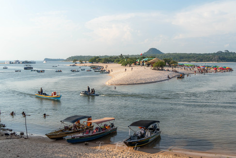 Ilha do Amor, Alter do Chao, Brazil. Sandy island in the Tapajos river with boats and people. The island is crowded with beachgoers under umbrellas. The sky is partly cloudy, creating a relaxed vibe.