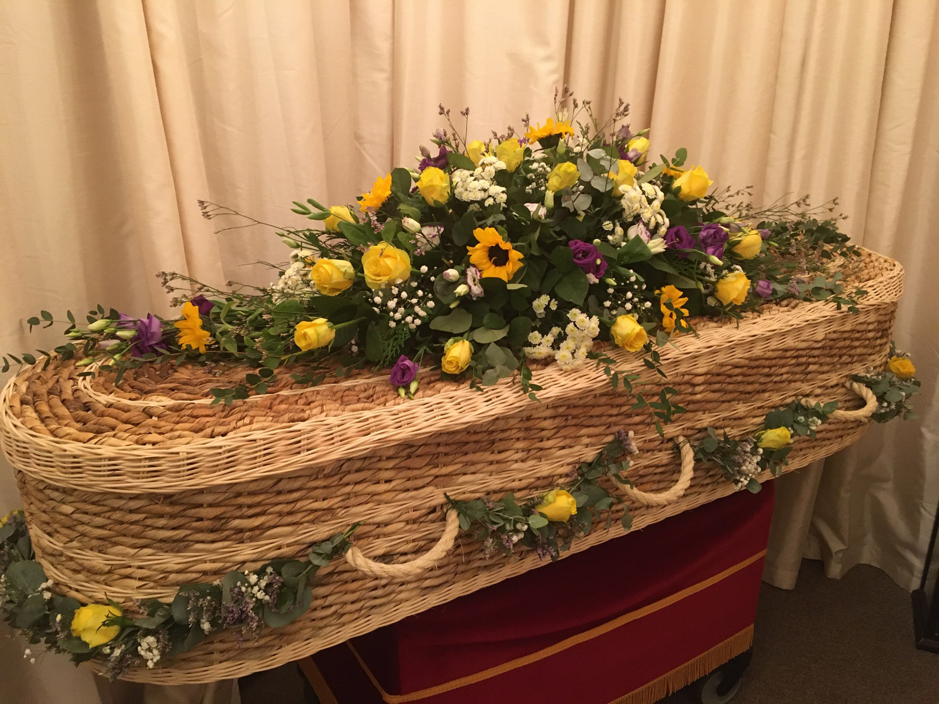 Wicker coffin with yellow and purple floral arrangement
