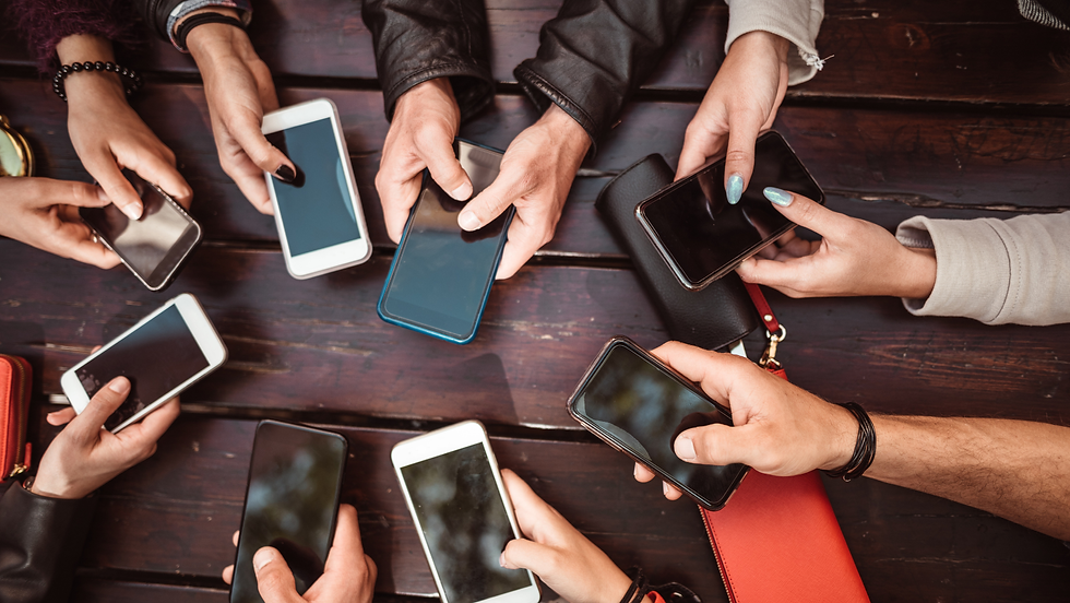 Hands of several people holding smartphones around a wooden table, suggesting group texting or browsing.