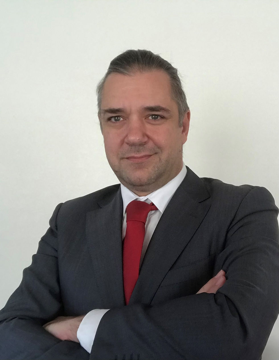 Smiling professional man with short hair wearing dark suit with a red tie posing confidently with arms crossed