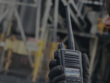 Female worker using two way radio communication at industrial site wearing safety gloves and glasses